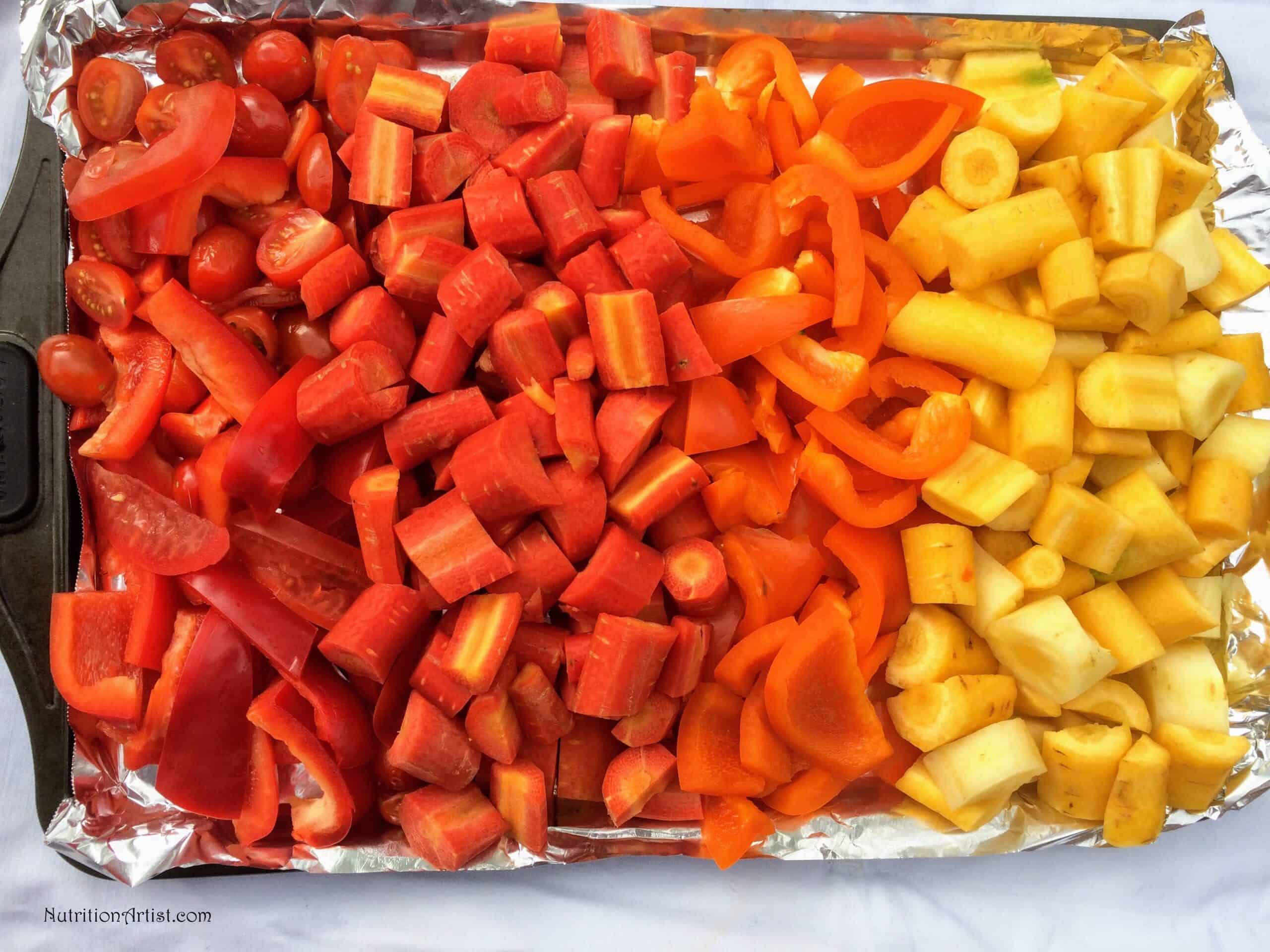 raw red, orange and yellow vegetables - grape tomatoes, bell peppers and heirloom carrots on a baking sheet. 