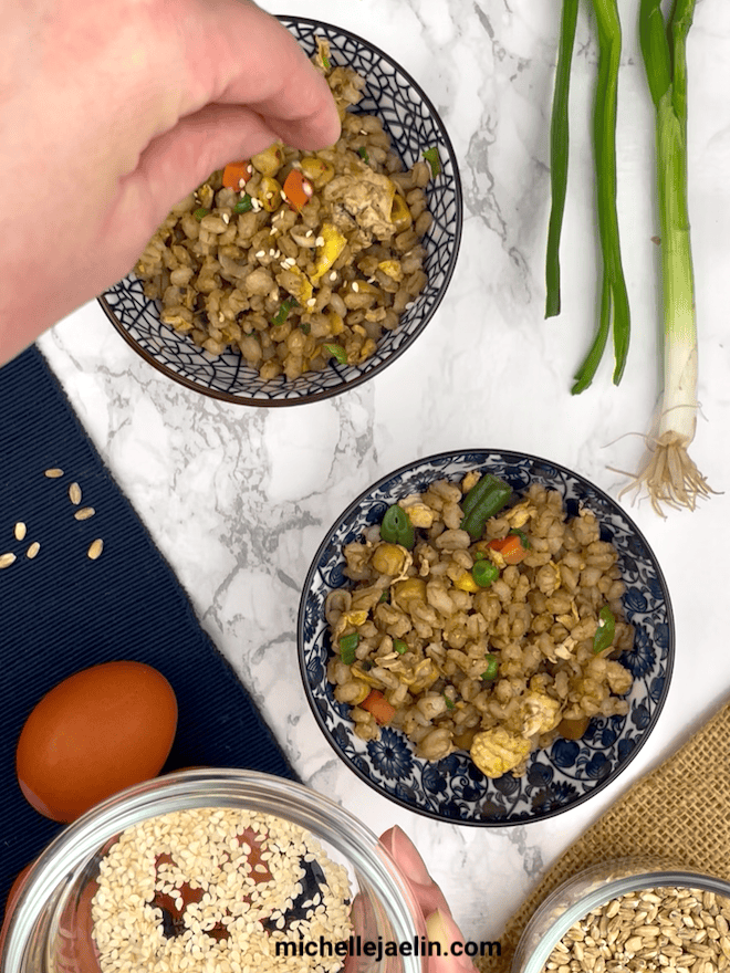 barley fried rice recipe in two bowls being topped with sesame seeds