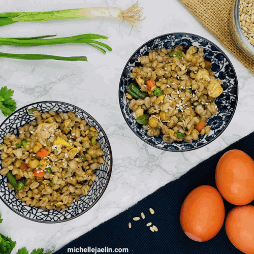 barley recipe in two bowls surrounded by eggs, raw barley, green onions and cilantro.