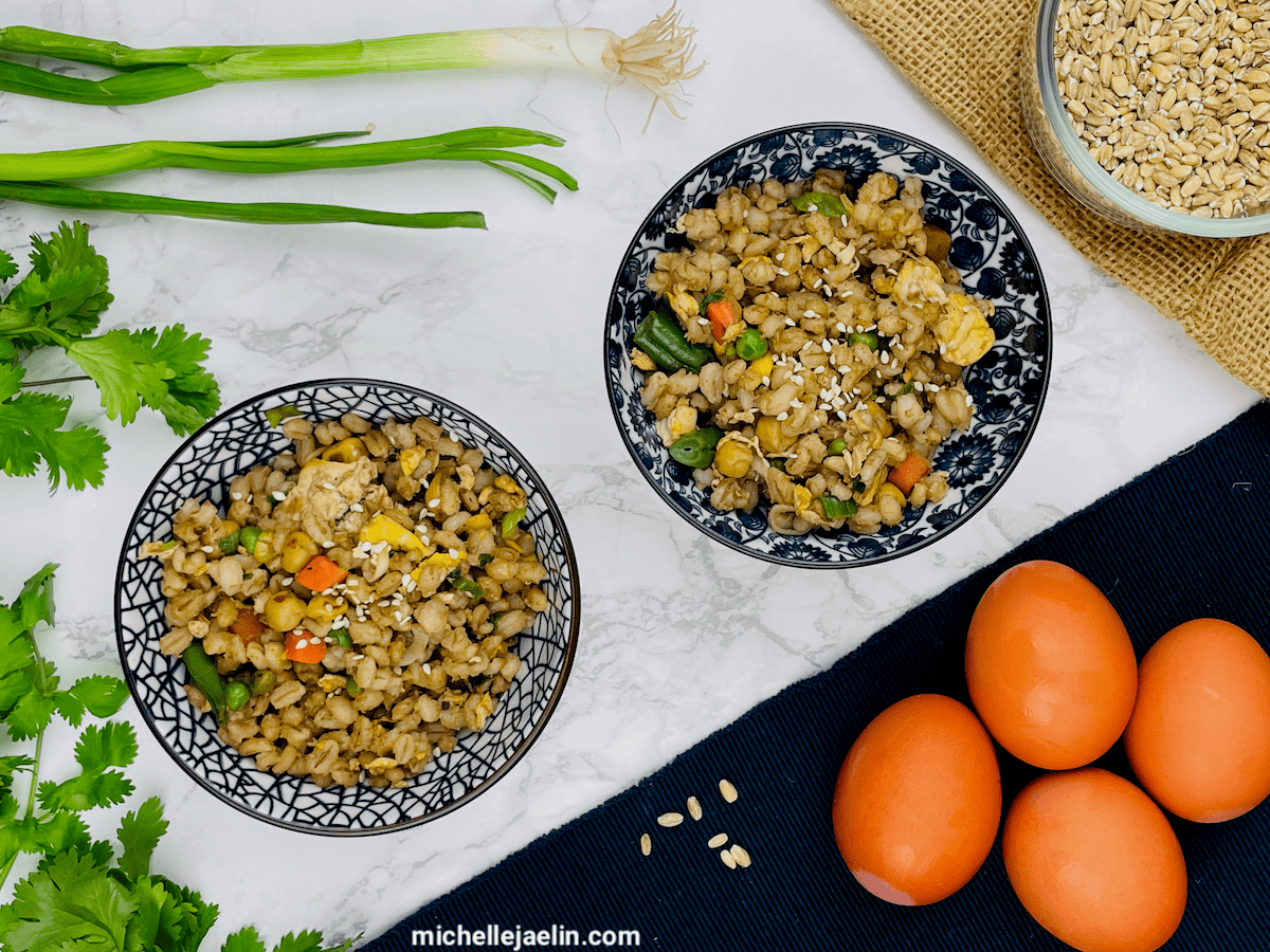 barley recipe in two bowls surrounded by eggs, raw barley, green onions and cilantro.
