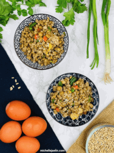 barley fried rice recipe in two bowls surrounded by eggs, cilantro, green onions and uncooked barley.