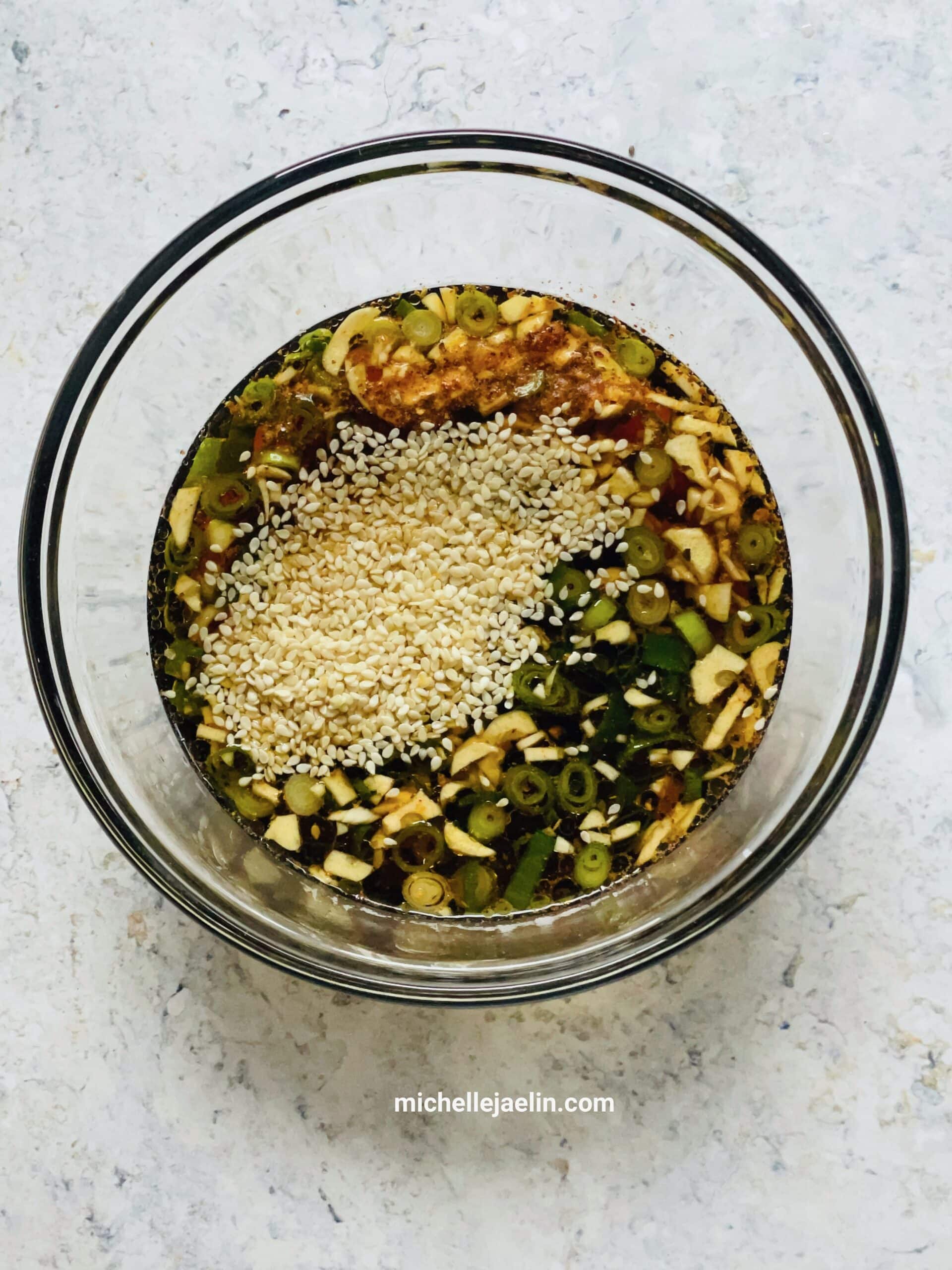 glass bowl with all marinade ingredients: garlic, green onion, chili flakes, soy sauce, honey, vinegar, water and sesame seeds.