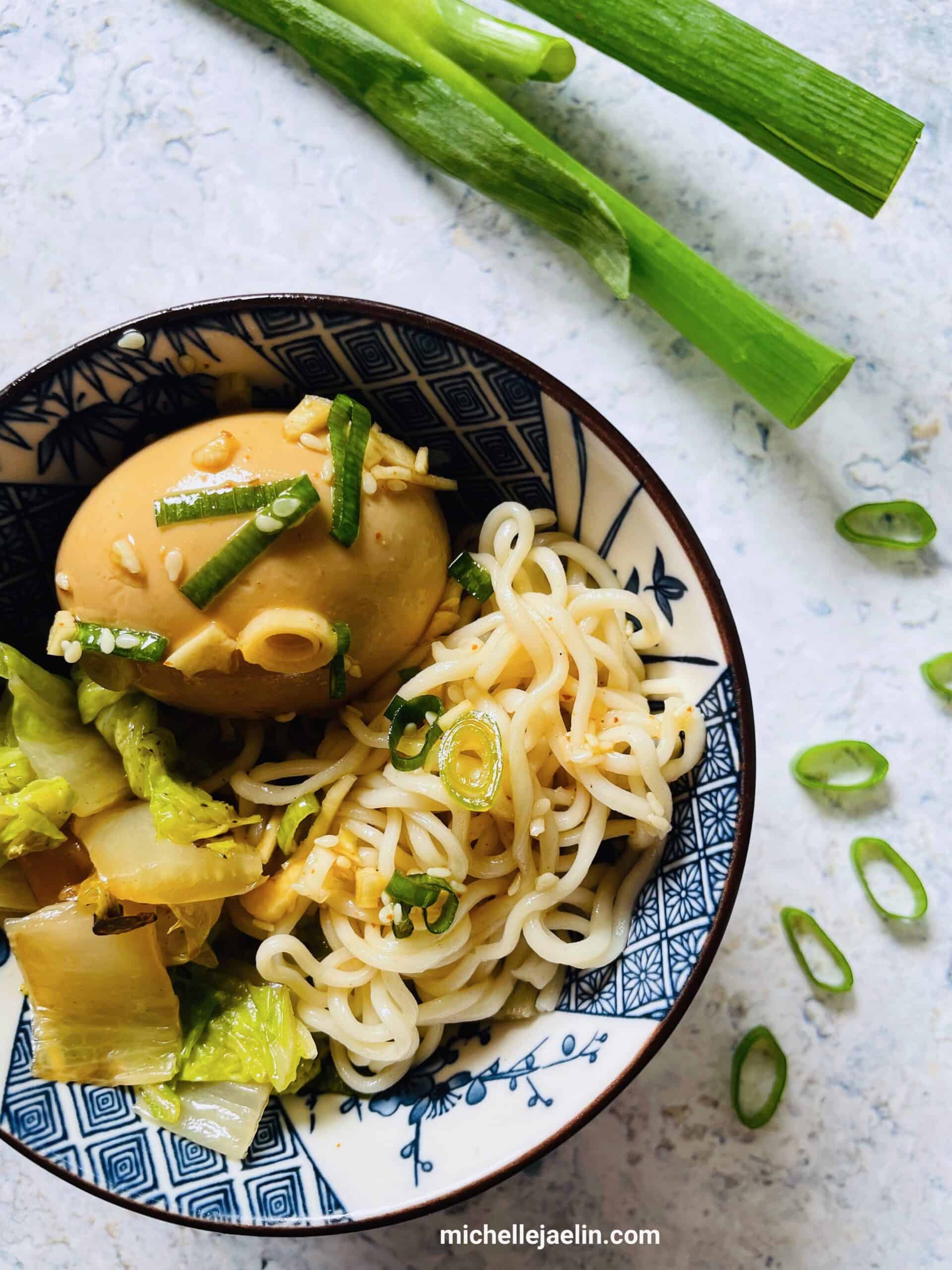 marinated boiled egg with bok choy and noodles in a bowl. Green onions on the side