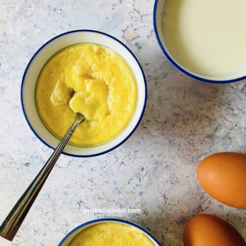 Chinese egg custard dessert recipe in 2 bowls with ingredients milk and brown eggs on the side