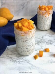overnight oats with mango recipe in 2 mason jars with 2 mangos in the background
