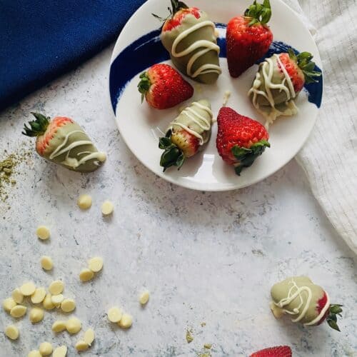white chocolate matcha covered strawberries on a plate surrounded by ingredients