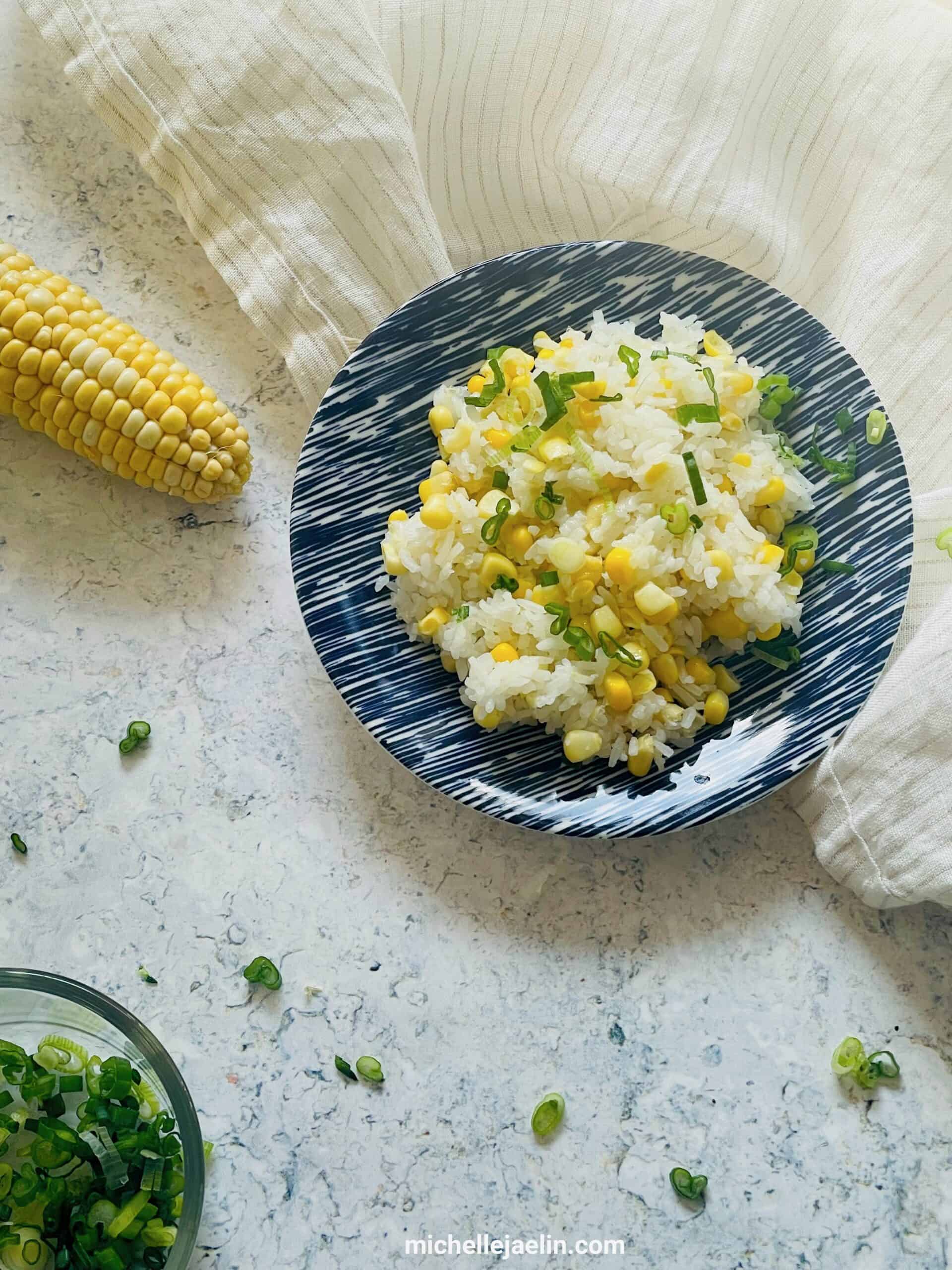 cooked rice and corn on plate with cob of corn and chopped green onion on the side.