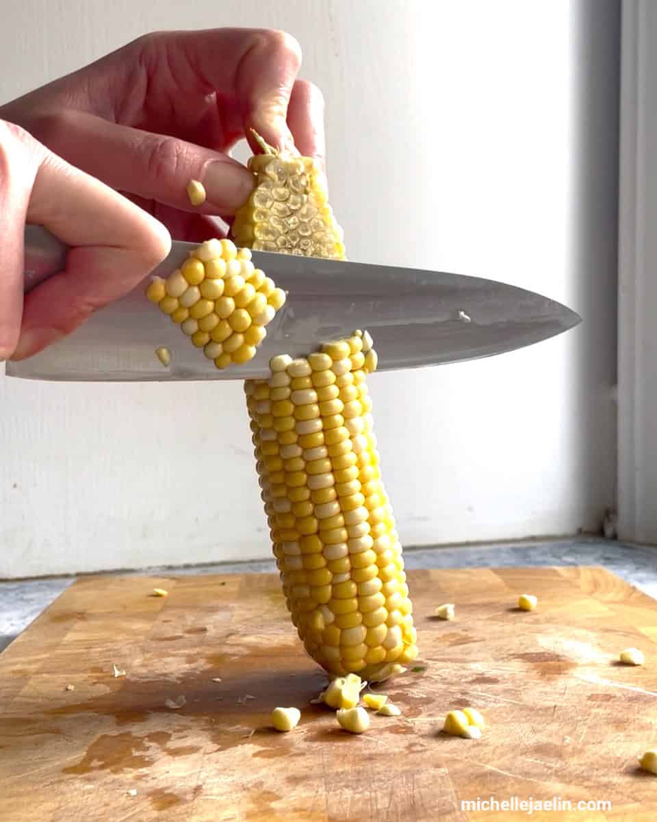 Corn cob being cut on wood cutting board 