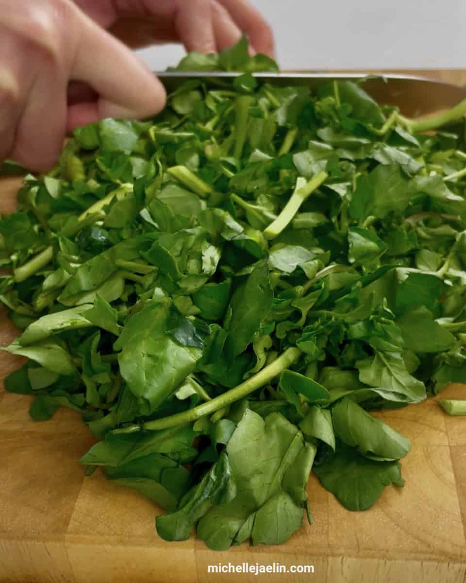 Close up of watercress being chopped on a cutting board