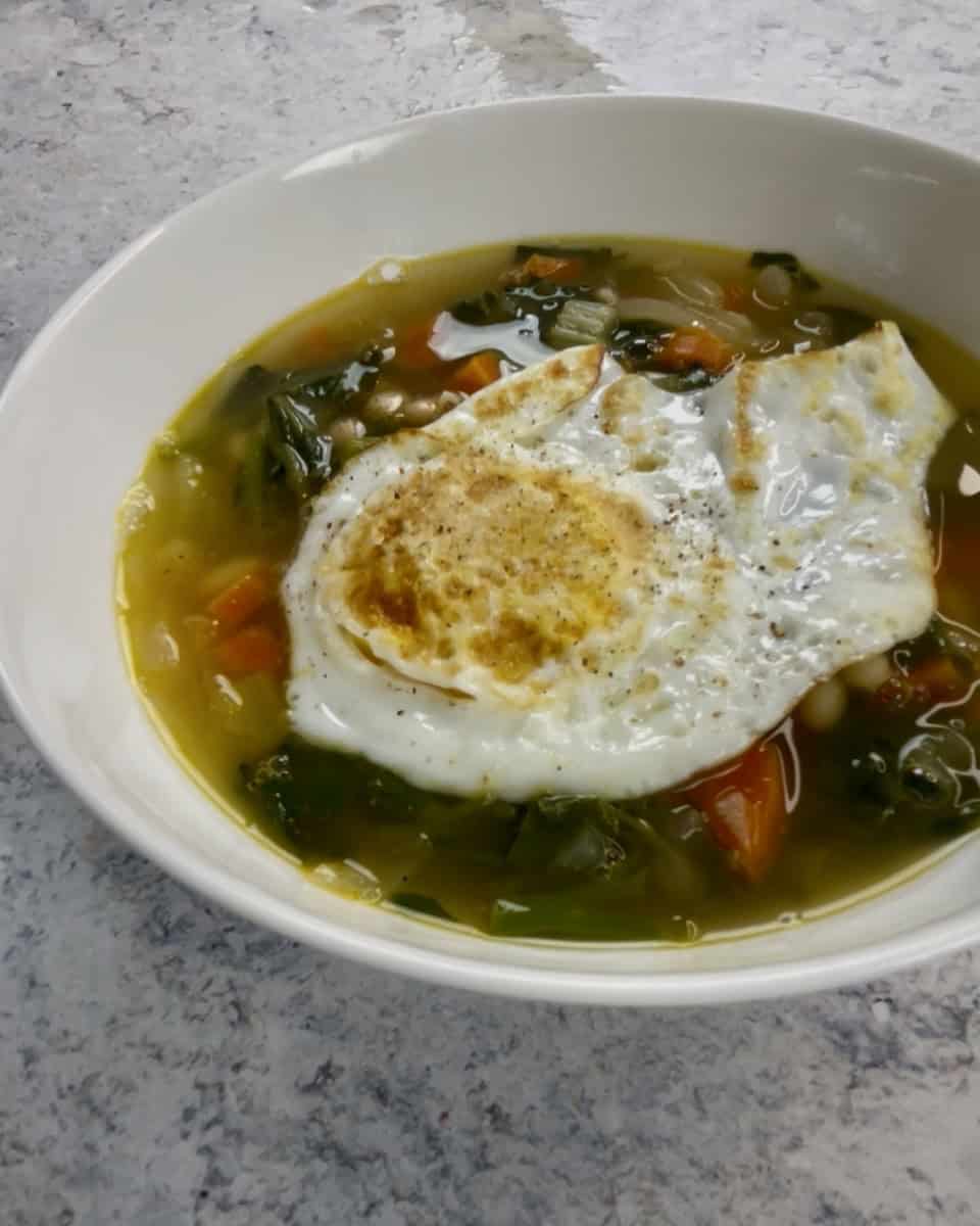 A fried egg in a bowl of beans and watercress greens soup
