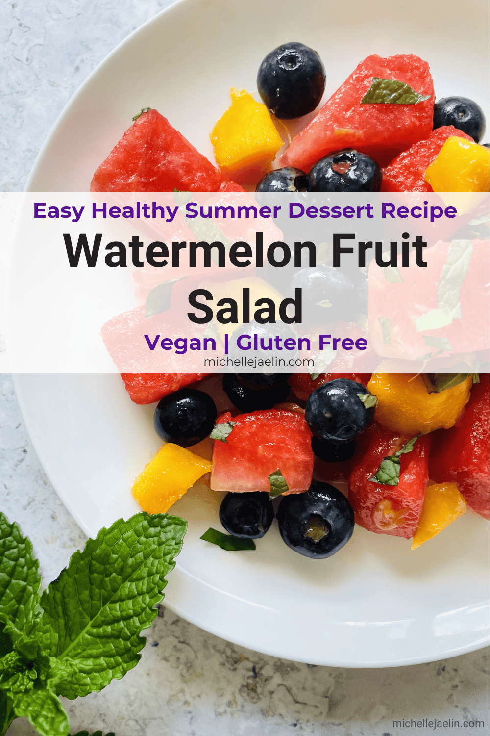 Watermelon Fruit Salad with mango and blueberries on a white plate with fresh mint in the bottom left hand corner and text on top - Pinterest photo 